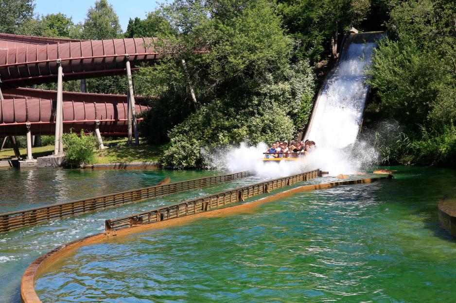 People on a water ride plunge down a ramp into a pool, creating a large splash.