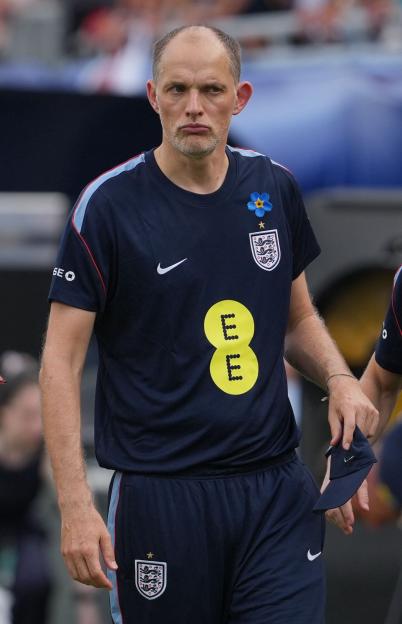 Thomas Tuchel wearing an England team shirt with sponsor logos and a blue flower pin.