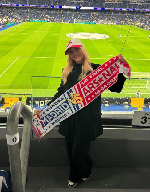 Laura Trossard Hilven holding a souvenir scarf at a soccer stadium.
