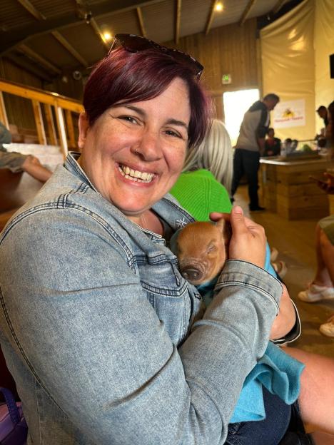 Tammy Downing, 44, smiling while holding a small piglet wrapped in a blue blanket.