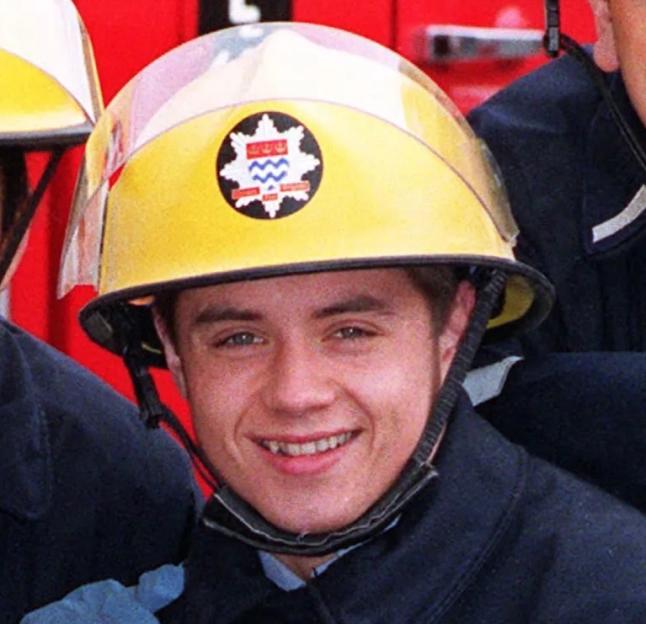 John Alford, who plays fireman Billy Ray in London's Burning, wearing a yellow fireman's helmet.