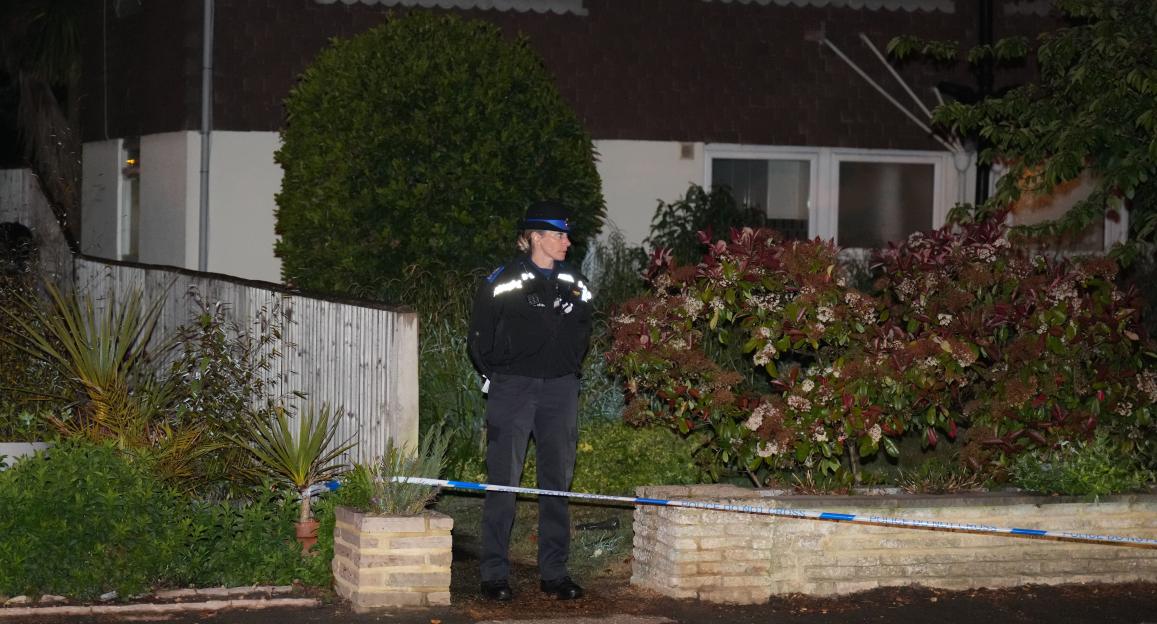 A police officer standing behind a "Police Do Not Cross" tape at a serious incident scene.