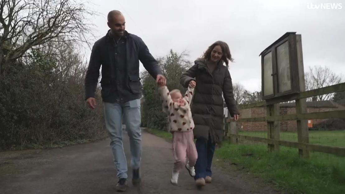 A young girl, Leni, is held by her parents as she walks.