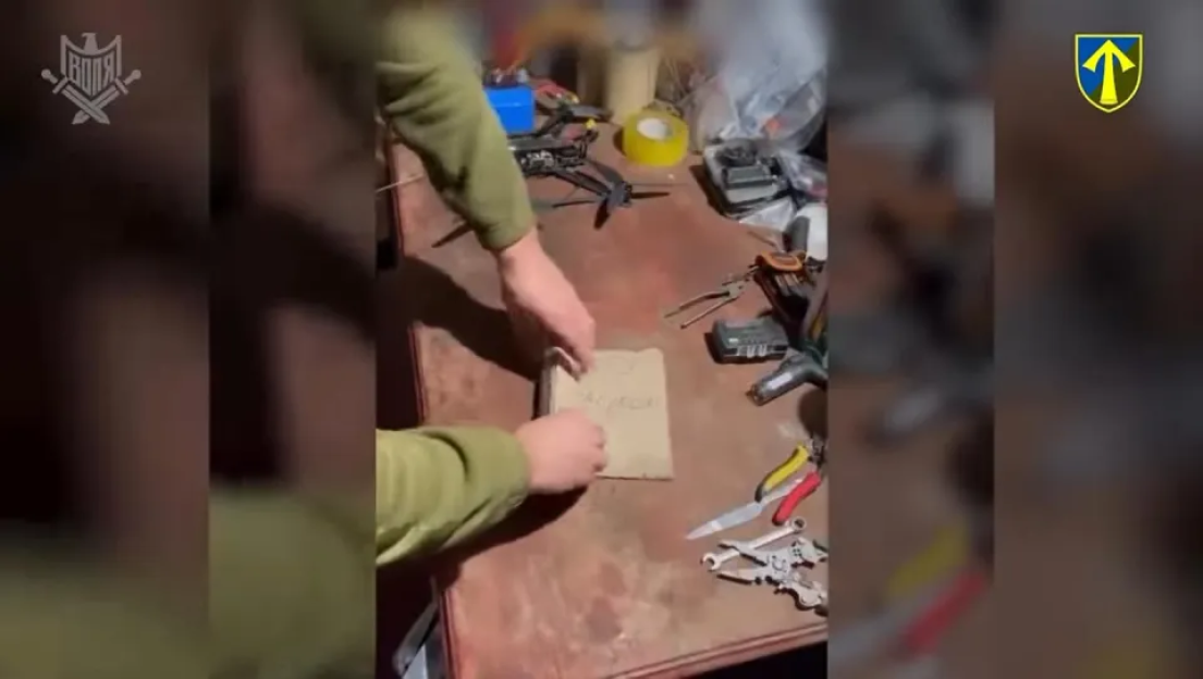 Hands placing a package on a table with tools and a drone.