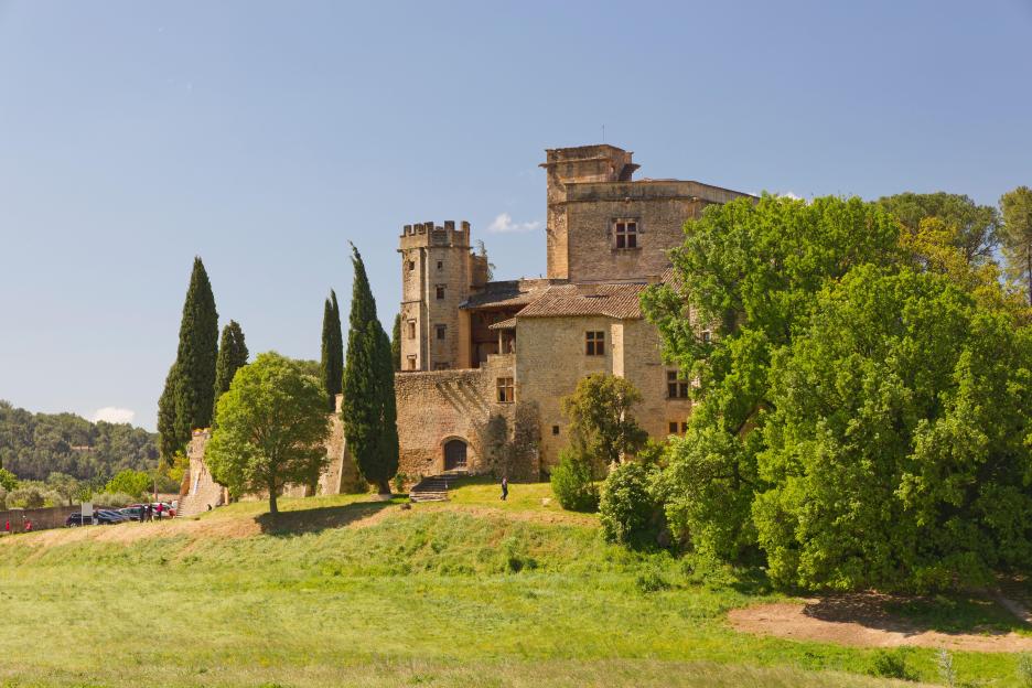 Château de Lourmarin, a 12th-century castle transformed in the 15th century, surrounded by trees on a sunny spring day.