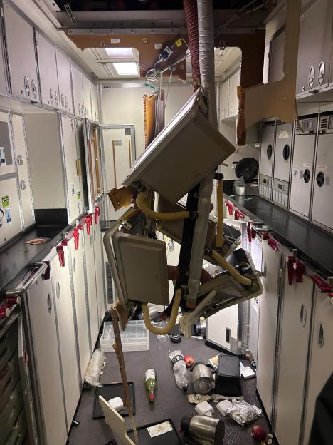 Airplane galley with debris strewn across the floor and ceiling panels hanging down after severe turbulence.