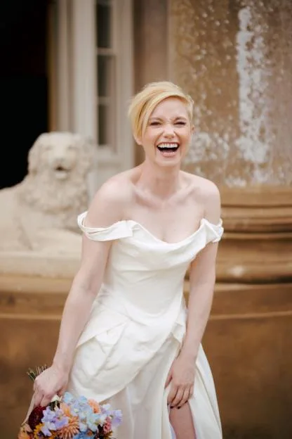 Bethany Heavens laughing in her wedding dress, holding a bouquet of flowers.