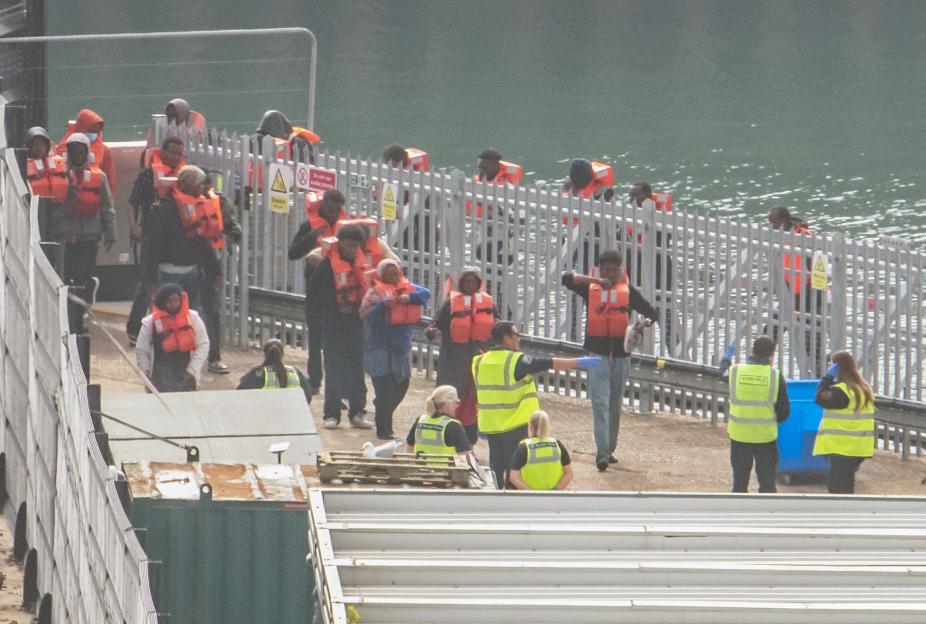 Migrants in orange life vests are escorted by Border Force personnel in yellow vests at Dover Docks.