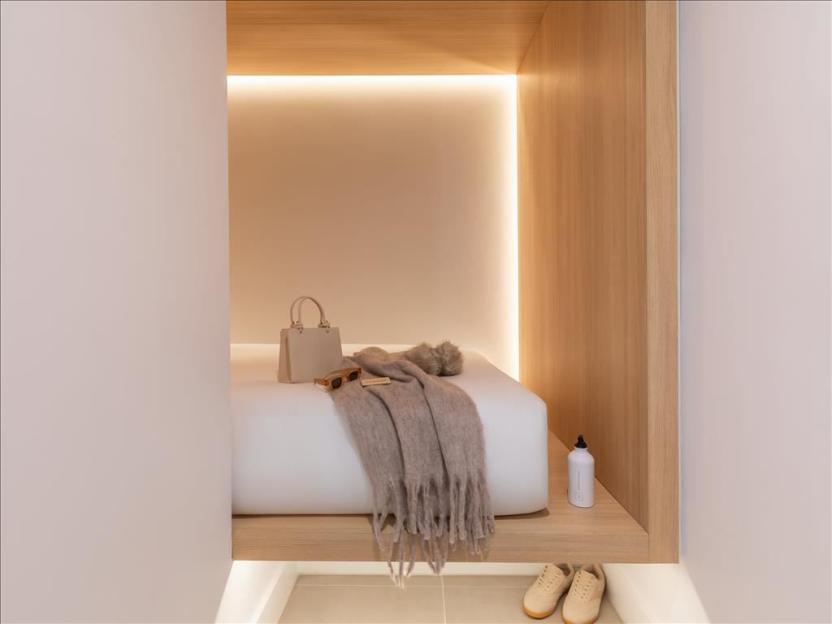 A minimal Zedwell Park Lane hotel room with a bed set into a wooden frame, a purse and blanket on the bed, and shoes on the floor.