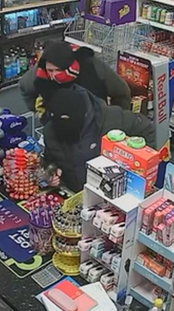 Two men wearing balaclavas in a shop, possibly during a robbery.