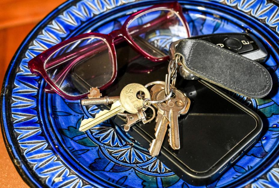 A close-up of a blue decorative plate holding eyeglasses, keys, and a mobile phone.