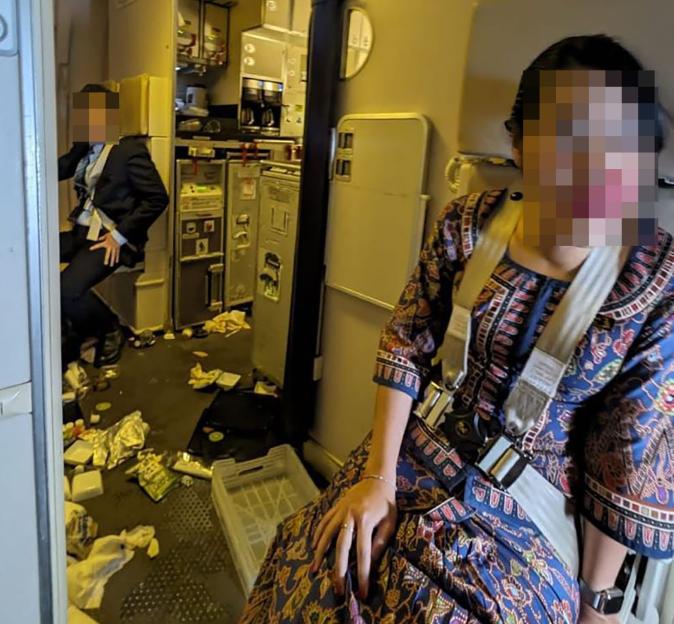 Cabin of a Singapore Airlines flight showing debris on the floor and a flight attendant belted into her seat, after severe turbulence.