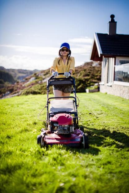 Woman mowing a lawn on a sunny day in Lauvoy, Norway.