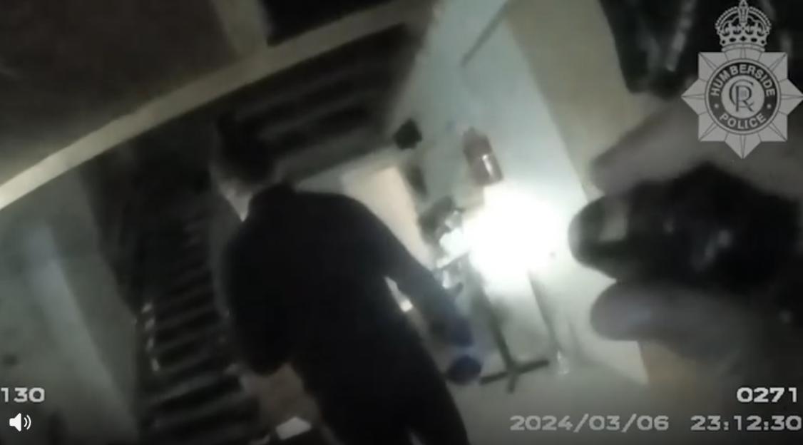 Humberside Police body camera footage showing an officer shining a torch into a messy room.