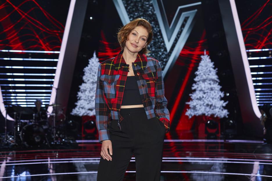 Emma Willis standing on the set of The Voice Kids, wearing a plaid jacket.