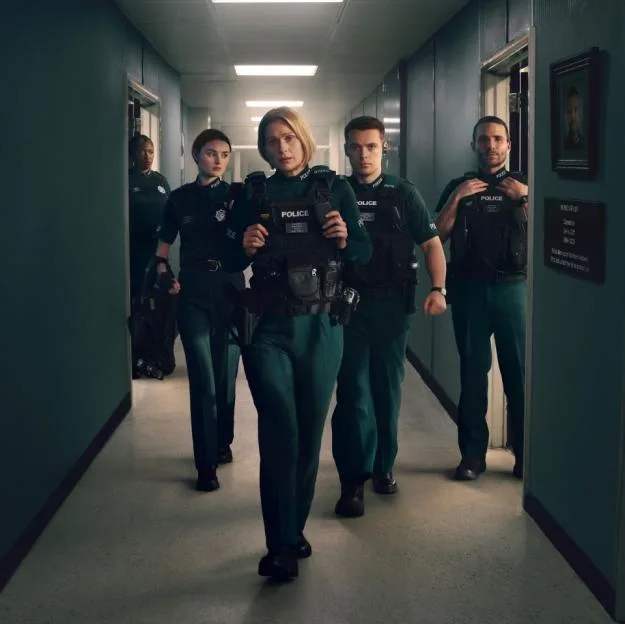 Five police officers in uniform walk down a hallway.