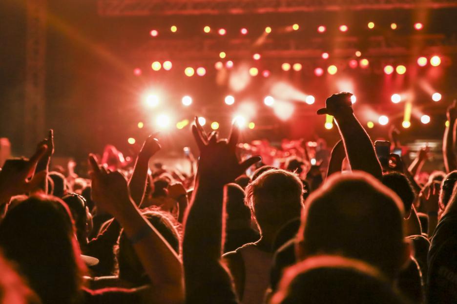 Concert audience with arms raised, lit by red stage lights.