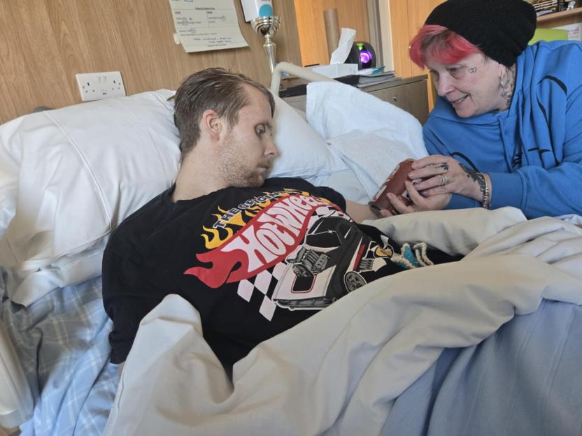 Samantha Fairbairn offering a drink to her son Andre in a hospital bed.