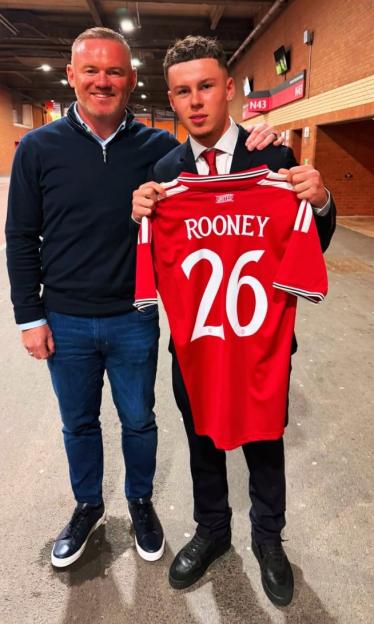 Wayne Rooney standing next to his son, who is holding a Manchester United jersey with "ROONEY 26" on the back.