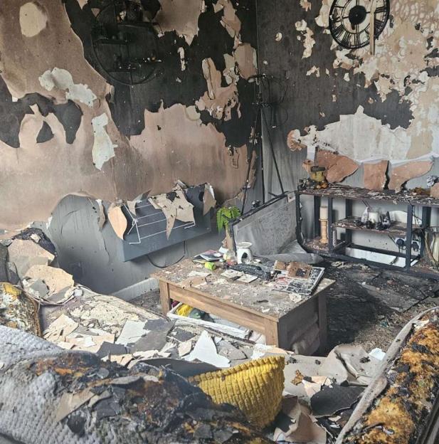 A living room in a home destroyed by fire, with charred walls, furniture, and debris.