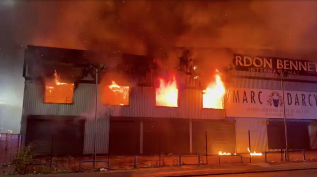 A building engulfed in a huge fire on a busy road.