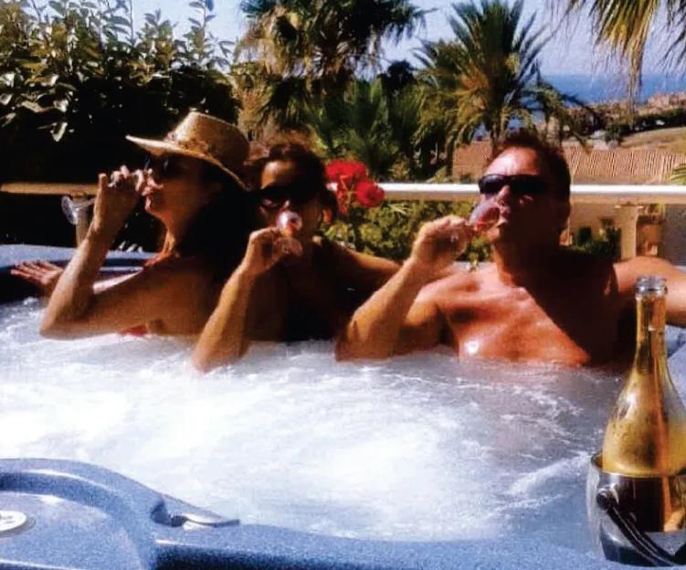 Three people in a hot tub, drinking from wine glasses, with a bottle of champagne in an ice bucket beside them.