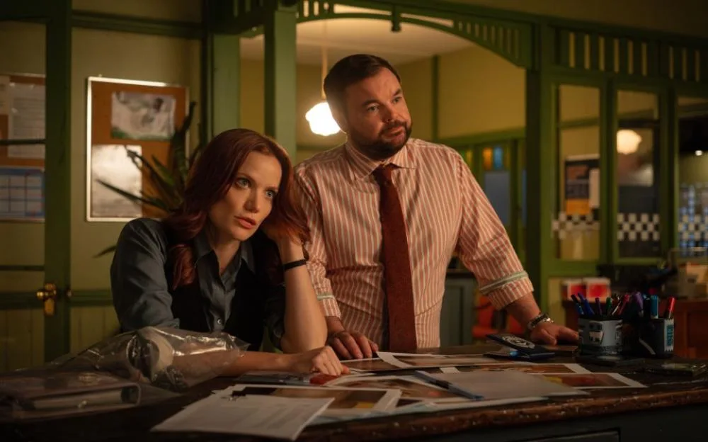 DI Mackenzie Clarke (Anna Samson) and Detective S.C. Colin Cartwright (Lloyd Griffith) looking at papers on a desk.