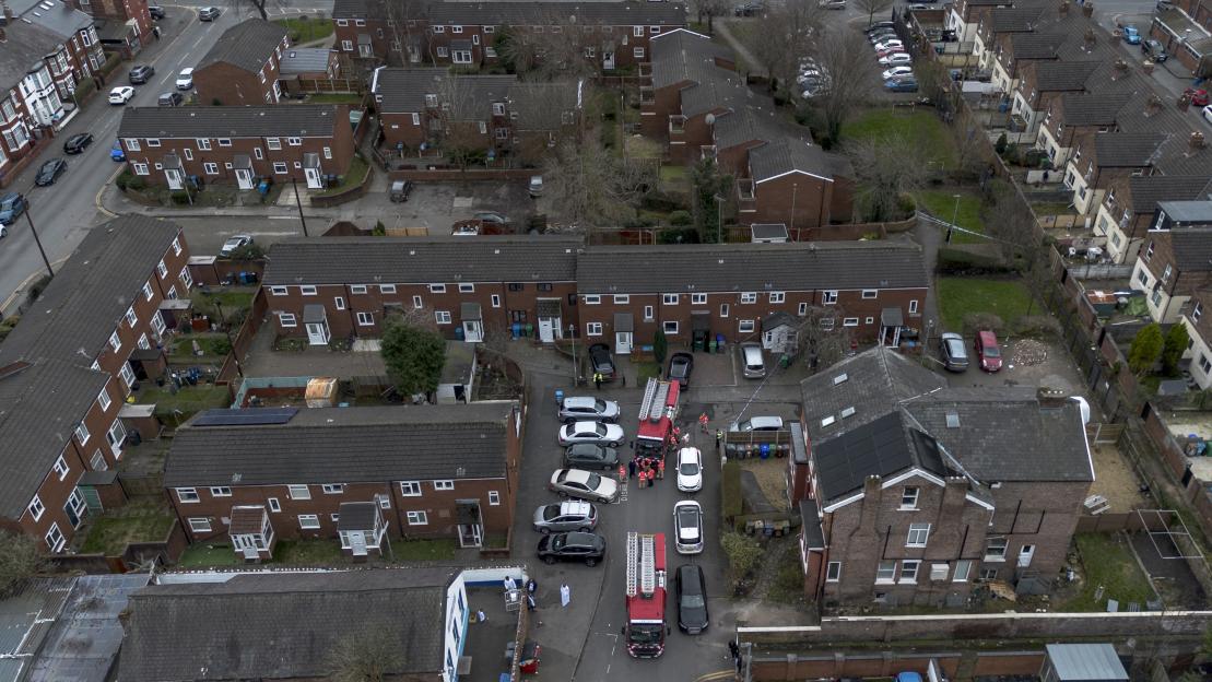 Aerial view of a street lined with two-story brick houses, with fire trucks and emergency personnel present.