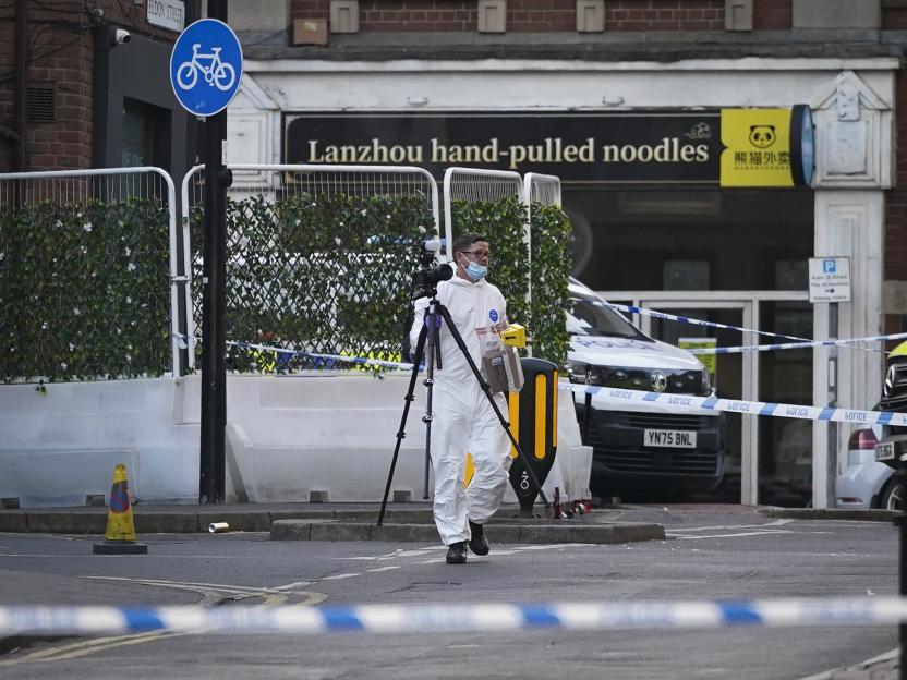 A forensics officer in a white protective suit and mask uses a camera on a tripod at a shooting crime scene in Sheffield, UK.