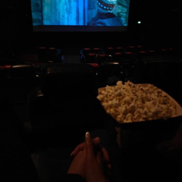 Two people holding hands while watching a movie in a dark theater, with popcorn in the foreground.