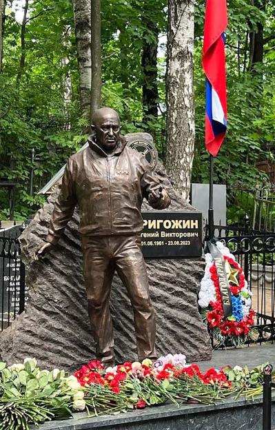 The grave of Yevgeny Prigozhin, featuring a bronze statue of him, flowers, and a Russian flag.