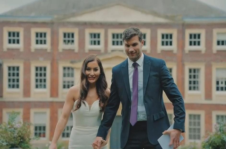 A newly married couple holding hands, walking in front of a brick building.