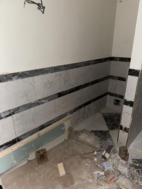 An unfinished bathroom with black and white tiles, exposed drywall, and construction debris on the floor.