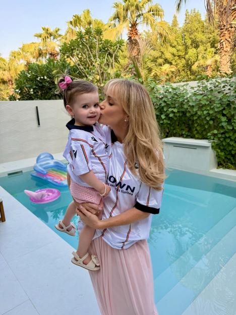 Laura Anderson wearing an Aberdeen football shirt and kissing a baby in a matching shirt by a pool.