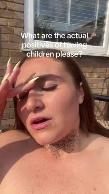 Woman with a neck tattoo looking annoyed while asking about the positives of having children.