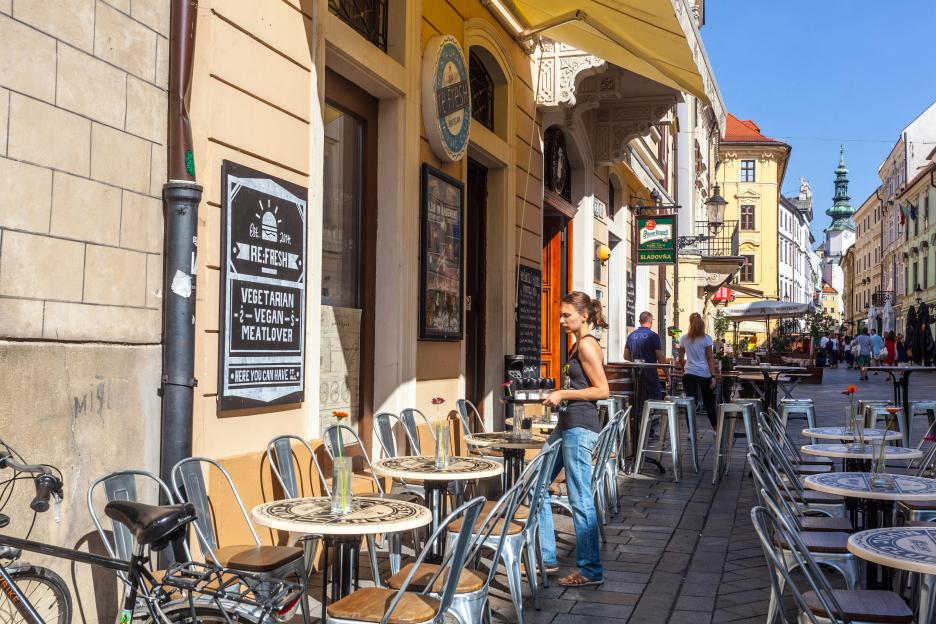 A woman carrying a tray on Michalska street in Bratislava Old Town, Slovakia, with outdoor seating for bars and cafes.