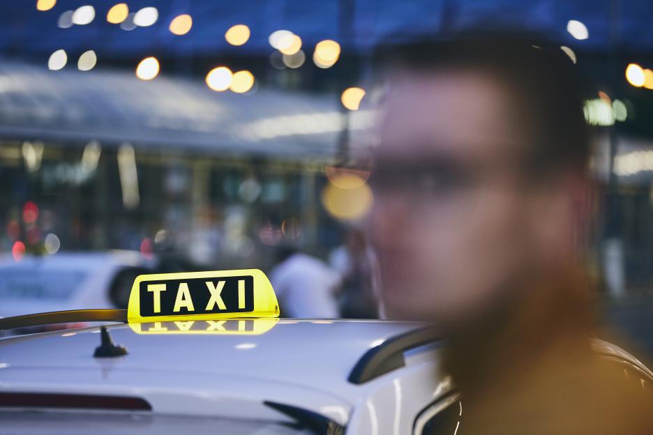 Close-up of a taxi sign on a car with a blurry person in the foreground, waiting at night.