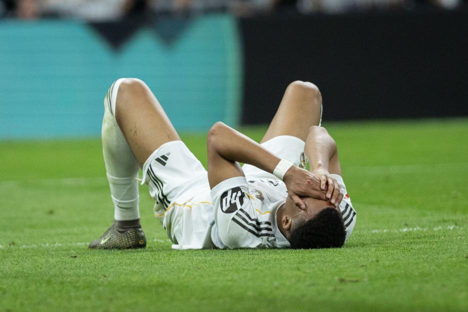 A Real Madrid player lying on the ground covering his face with his hands, visibly upset.