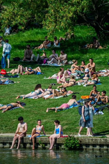 People relaxing on the grassy banks of Hampstead Heath Ponds on a sunny day.