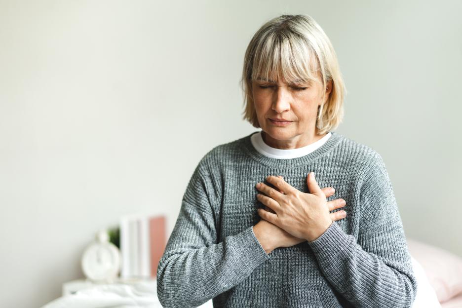 Woman with short blonde hair and closed eyes pressing both hands to her chest in pain.