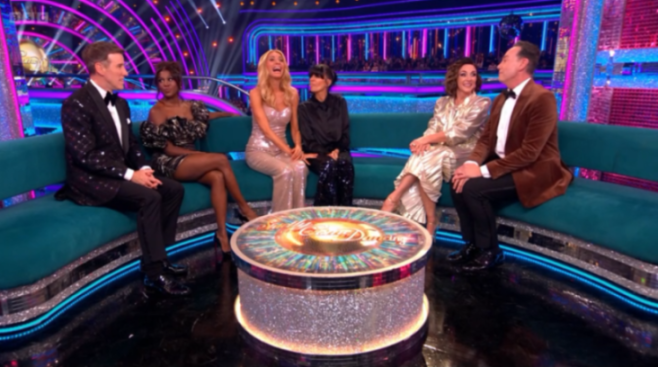 Five people, three women and two men, sit on a blue sofa around a sparkling round table with the Strictly Come Dancing logo.