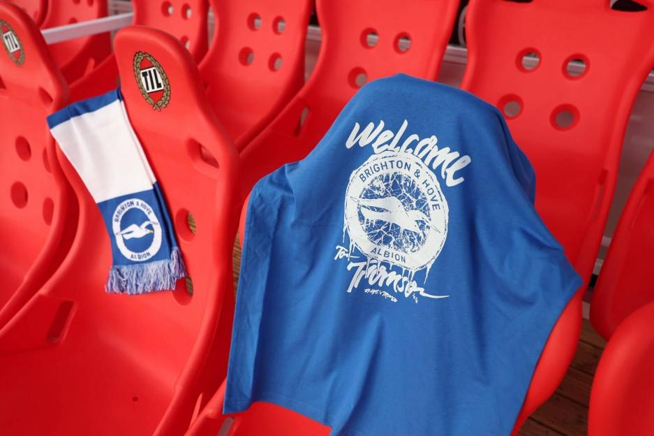 A blue Brighton & Hove Albion t-shirt and scarf on red stadium seats.