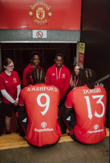 Manchester United players Rashford and Dorgu sitting on steps with young people from the Manchester United Foundation.