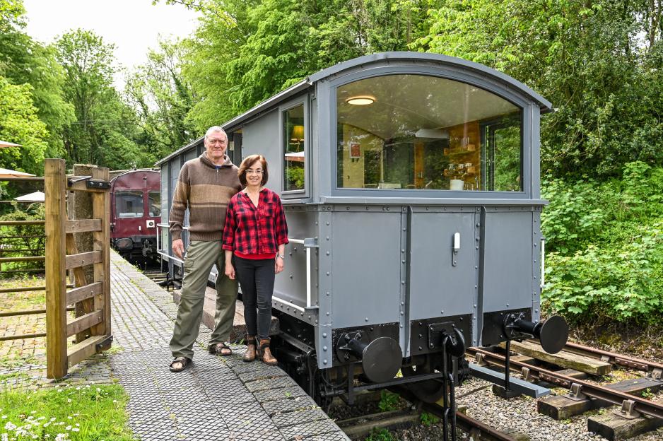 Cecilia Chavez-Brandon and Paul Kirwan standing next to a restored gray train car on a railway platform.