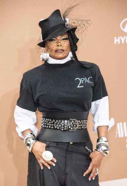 Janet Jackson at the BET Awards in a black fedora with a net veil, black "2PAC" t-shirt over a white shirt, wide black belt, and black pinstriped pants.