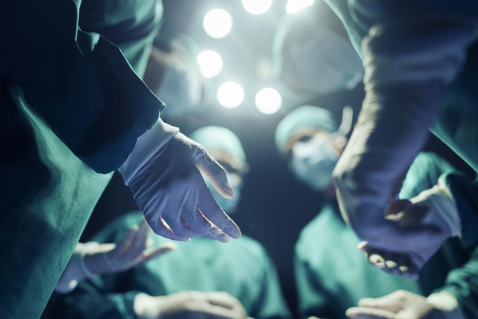 Four surgeons in scrubs and masks, seen from below, discussing before an operation.