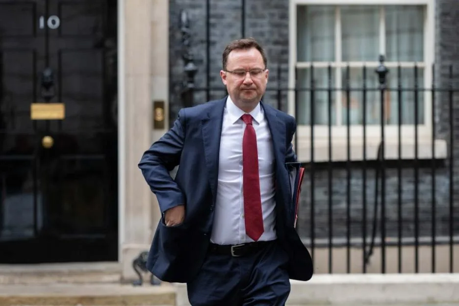 A man in a suit and red tie walking outside Number 10 Downing Street.