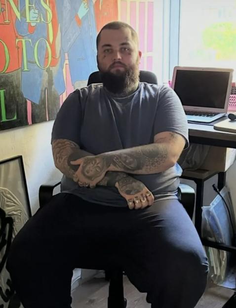 A man with a beard and tattoos sits in a chair, with text overlay reading "ozempic mounjaro made me hot."