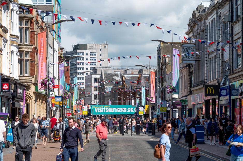 People walk along a street in Southend, UK, with banners and bunting overhead, and shops on either side.
