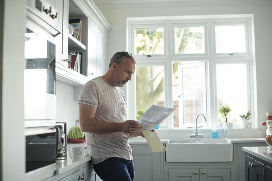 Man in a kitchen reading a document he's taken out of an envelope.